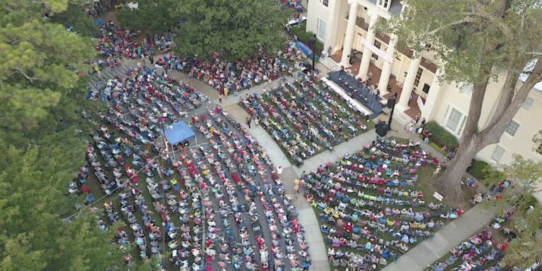 Aerial view of audience sitting in front of a stately building on the campus of Athens State University listening to musical performers.