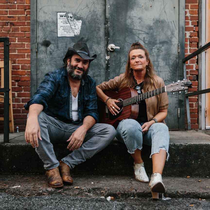 A man and woman sitting on a doorstep holding musical instruments.