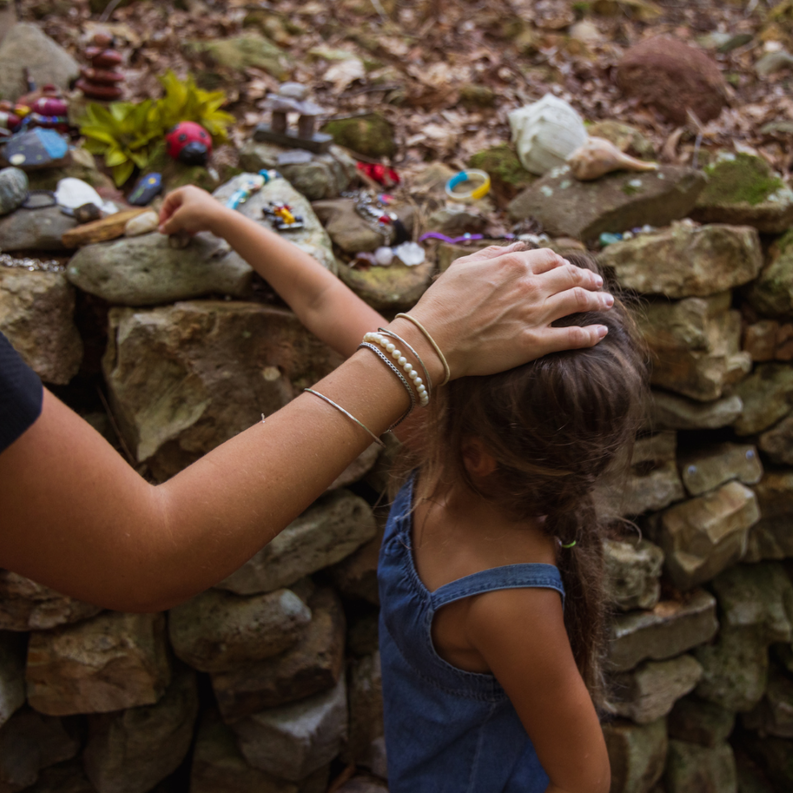 A mother's and child's hands putting memorial trinkets on top of a stone wall